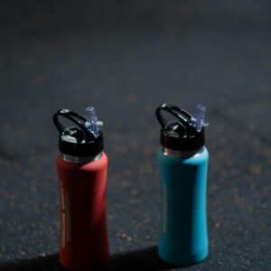 Two vibrant sports bottles on a dark textured floor, blue and red.
